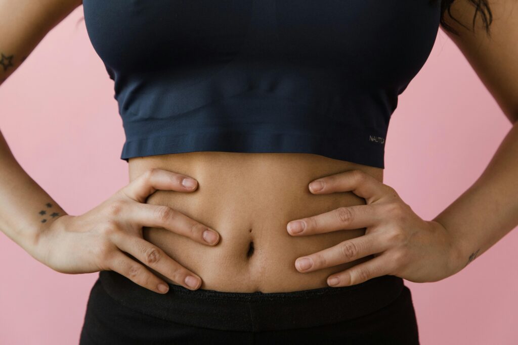 A close-up shot of a woman's toned stomach with hands on hips, against a pink background.